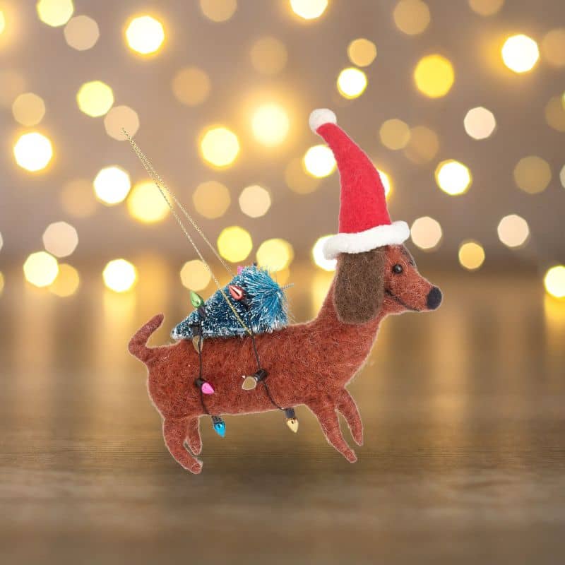 Boule de noël en feutrine qui représente un chien teckel avec un sapin et une guirlande la marque Sass and Belle à accrocher dans le sapin