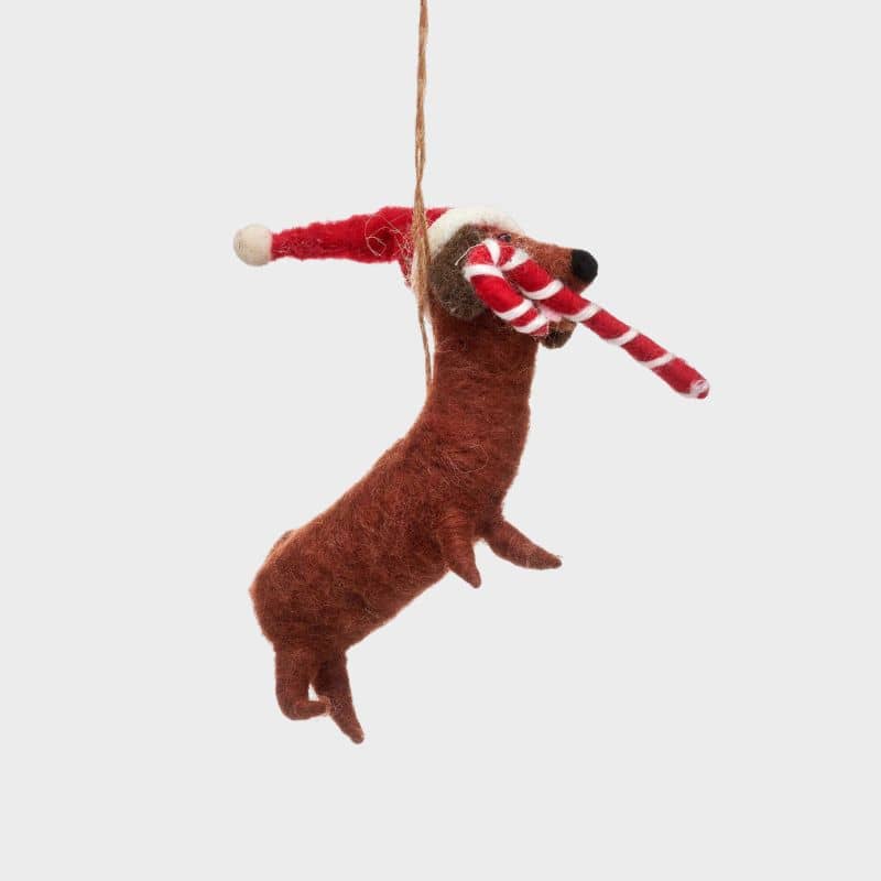 Boule de noël en feutrine qui représente un chien teckel saucisse avec une canne à sucre orge candy cane de la marque Sass and Belle